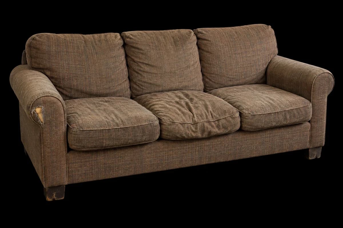 Worn three-seat sofa Old straight sofa with sagging cushions and a torn arm.